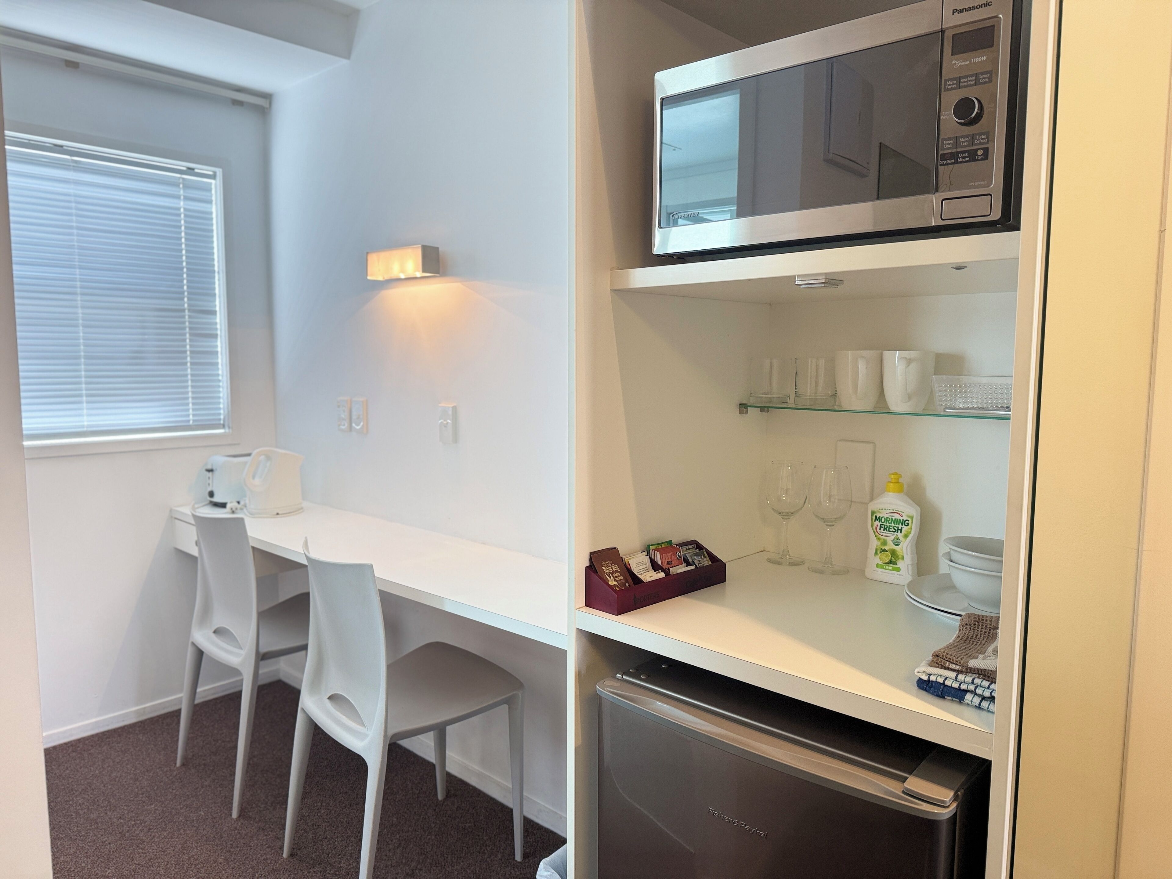 Una kitchenette compacta con microondas, refrigerador y un pequeño comedor con una silla y mesa.