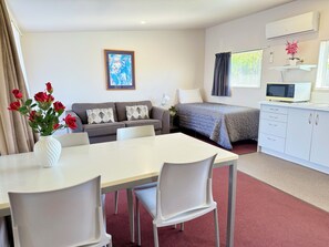A modern hotel room with a dining area, a sofa set, a bed, a small kitchenette, and a painting on the wall. - Morrinsville Motel (Morrinsville)
