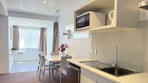 A modern kitchen with a microwave, sink, and cabinets. There is a dining area with chairs and a table, and a window with curtains. - Morrinsville Motel (Morrinsville)