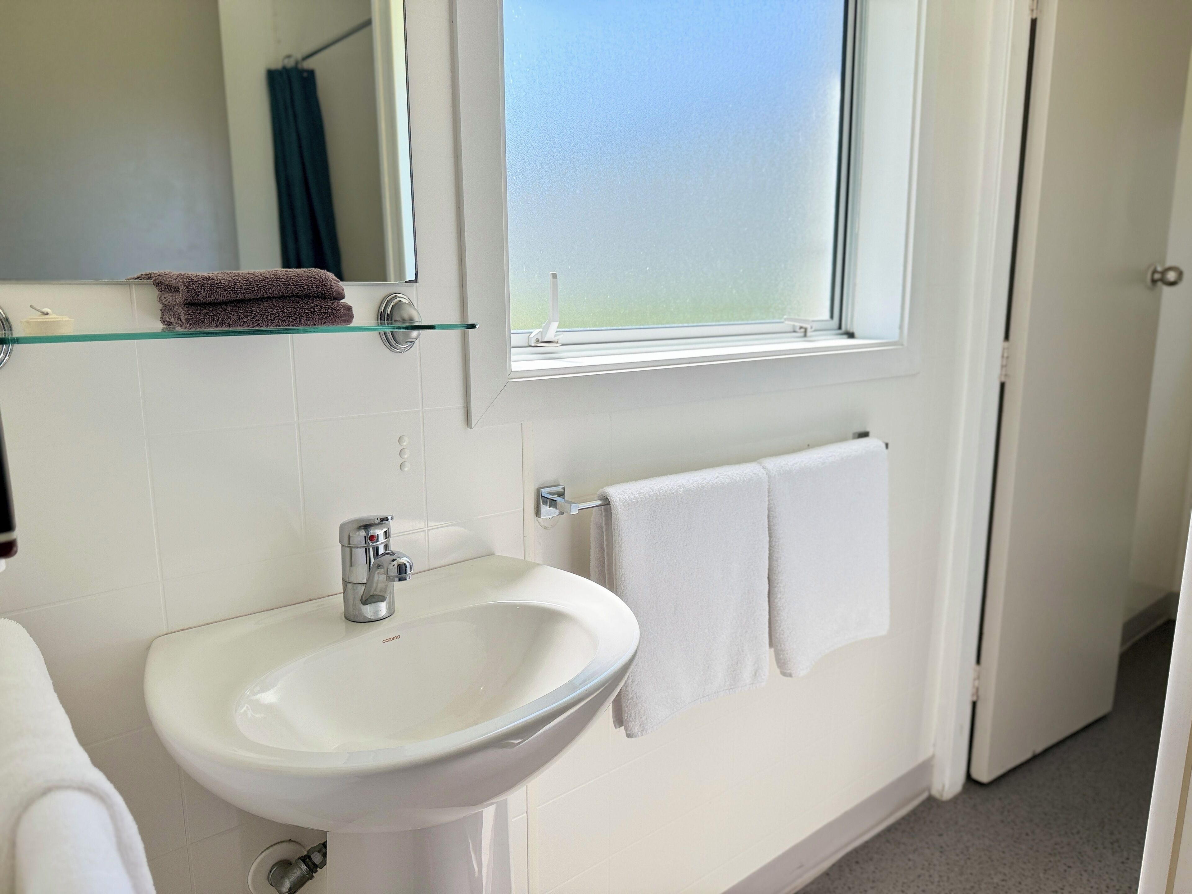 A bathroom with a white sink, a mirror, and a window.