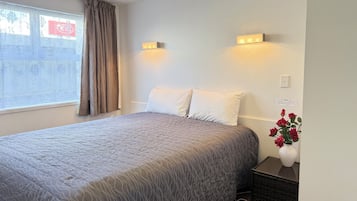 A hotel room with a bed, a nightstand, a vase with flowers, and a window with curtains.