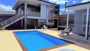 A modern two-story building with a swimming pool, outdoor seating, and a covered patio area. - Morrinsville Motel (Morrinsville)