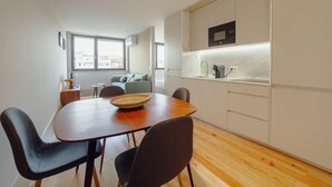 A modern kitchen with white cabinets, a wooden dining table, and chairs. - Legacy Oporto Design Apartment G by Vacationy (Porto)
