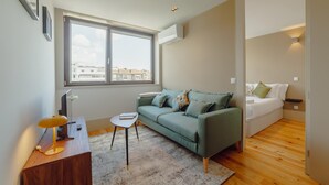 A modern living room with a green sofa, a small side table, a lamp, and a view of the city through large windows. - Legacy Oporto Design Apartment G by Vacationy (Porto)