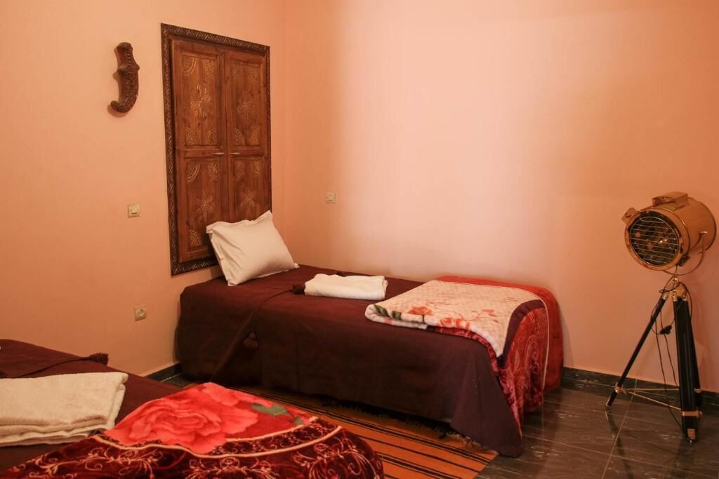 A room with two beds, a wooden wardrobe, and a vintage fan.