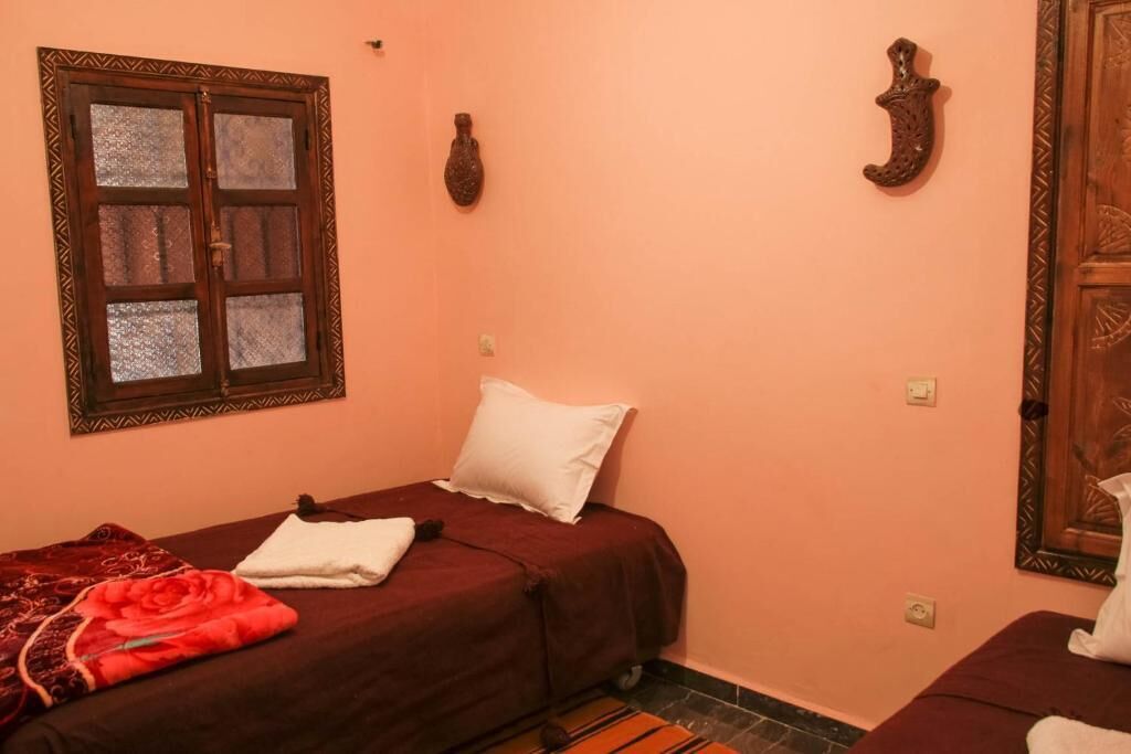 A bedroom with two beds, a window with a decorative frame, and a wooden door.