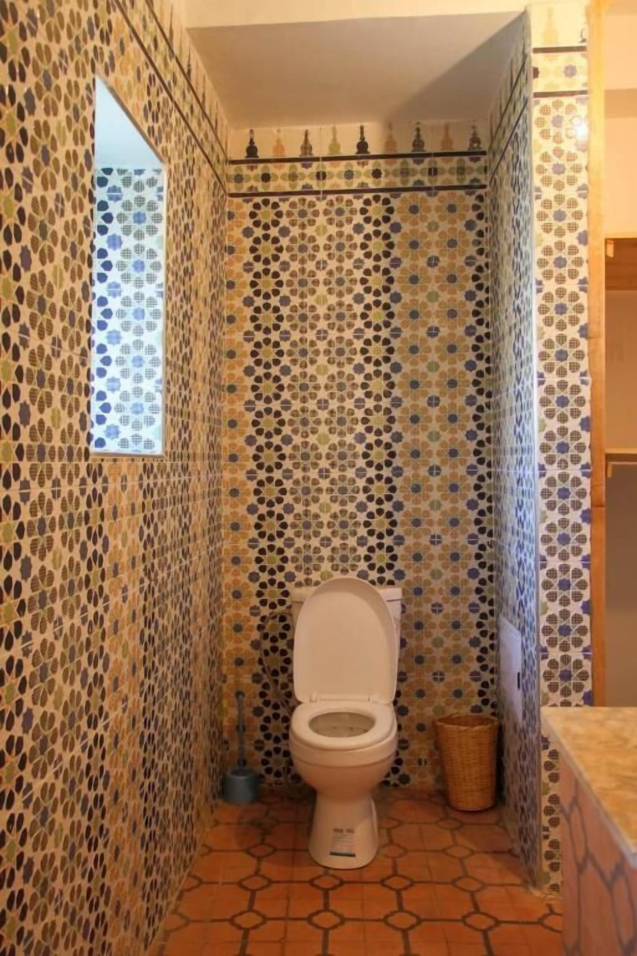 A bathroom with mosaic tile walls, a toilet, a small window, and a tiled floor.