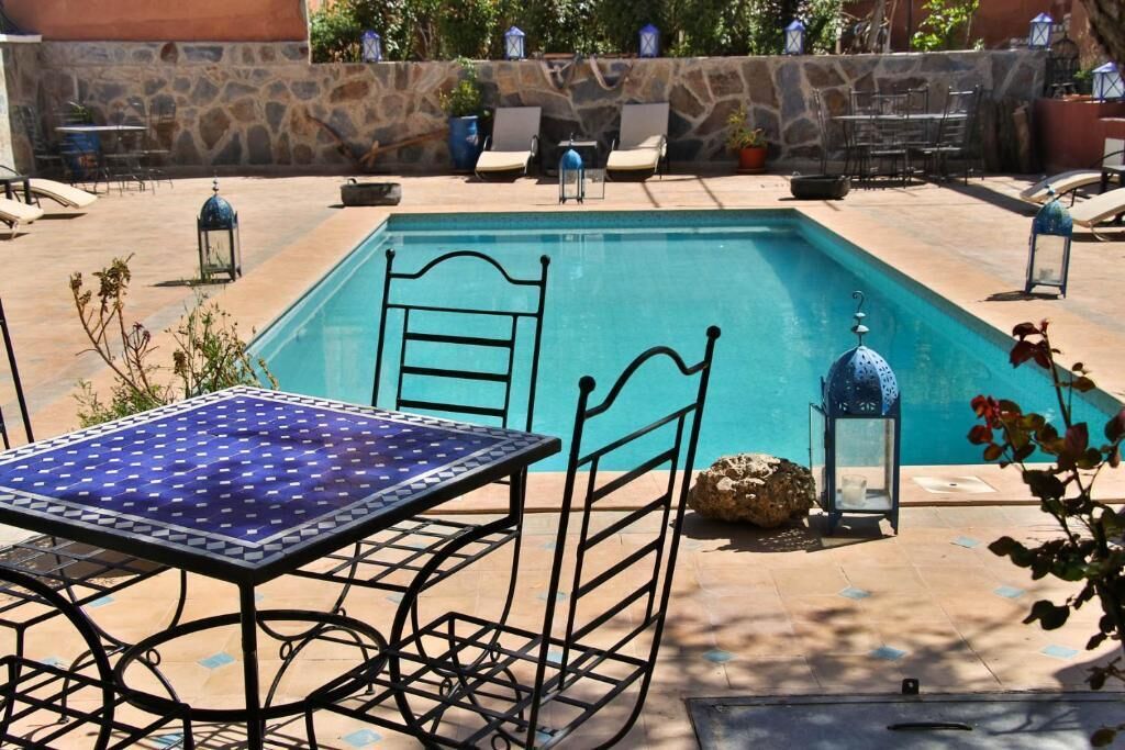 Une piscine avec une table et des chaises en métal, entourée de murs en pierre et de plantes en pot.
