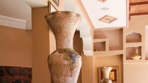Un vestíbulo de mármol con un jarrón grande, un vaso de leche y una mesita.