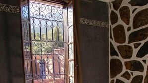 Una habitación con una cama, una ventana con rejas de metal, una pared de piedra y un suelo a cuadros.