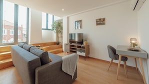 Ein modernes Wohnzimmer mit grauem Sofa, Fernseher, Esstisch und einer Pflanze.