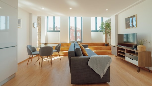 Ein modernes Wohnzimmer mit Sofa, Sesseln, Esstisch und Fernseher.