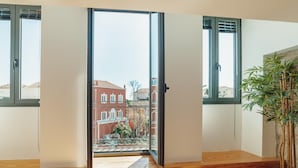 Ein Zimmer mit einer großen Schiebeglastür, die auf einen Balkon mit Blick auf ein rotbackiges Gebäude führt.