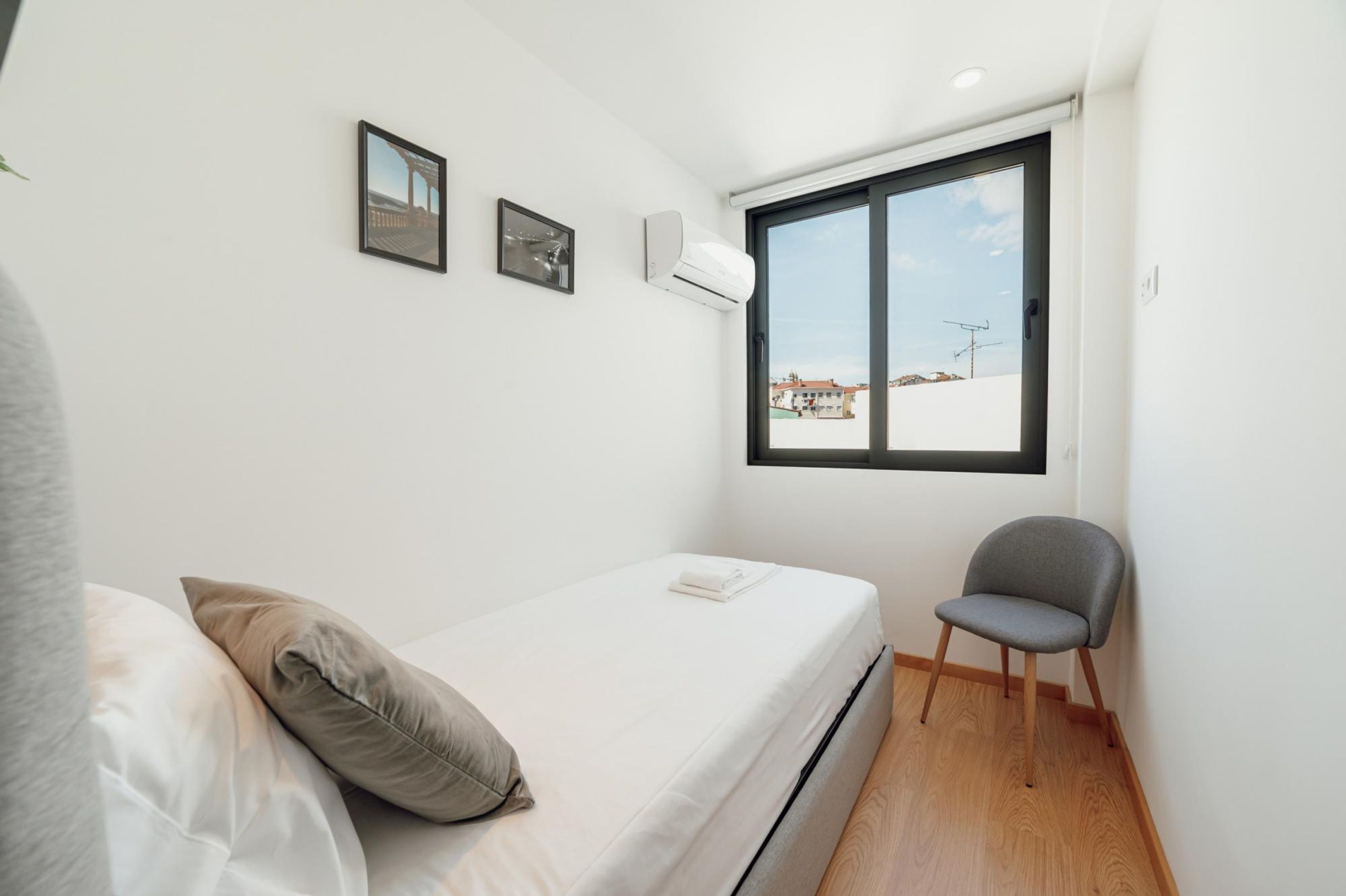 A small, modern bedroom with a single bed, a chair, and a large window offering a view of the outside.