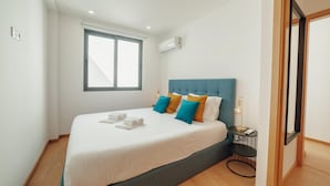 A modern hotel room with a large bed, a small side table, and a window with blinds.