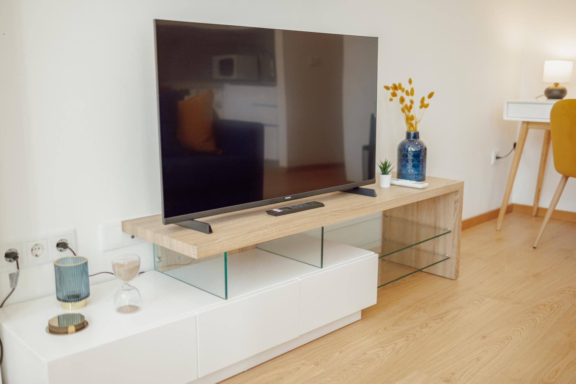 A modern living room with a flat-screen TV on a wooden console, a glass coffee table, and a small plant.