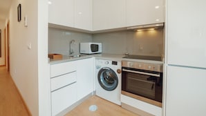 A compact kitchen with white cabinets, a microwave, a washing machine, and an oven.