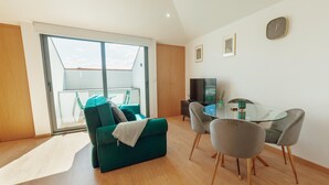 A modern living room with a green sofa, a glass dining table, and a TV.