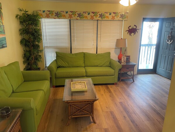 A living room with a green sofa, a glass coffee table, and a potted plant. - Reel Em Inn (Carrabelle)