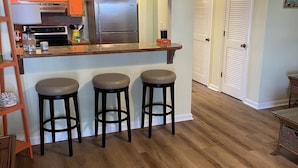 A kitchen with a refrigerator, a microwave, and a stove. There are three stools and a small table. - Reel Em Inn (Carrabelle)