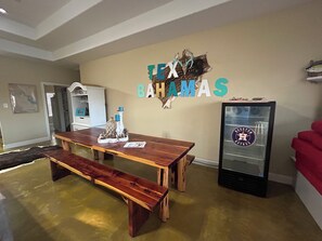 Un vaste salon comprenant une table à manger en bois, un banc, une vitrine en verre ornée d’un logo et un mur sur lequel est apposé un grand panneau avec une inscription.