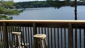 Eine Holzterrasse mit zwei Hockern mit Blick auf einen See, umgeben von Bäumen.