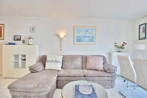 Ein Wohnzimmer mit einem beigefarbenen Ecksofa, einem weißen Korpus mit Glastüren, einem runden Couchtisch und einer wandmontierten Leuchte.