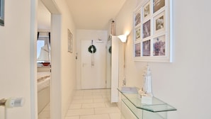 A hallway with a glass-top desk, a white door with a wreath, and framed pictures on the wall. - Seebrücke Appartement 14 - Seebrücke (Scharbeutz)