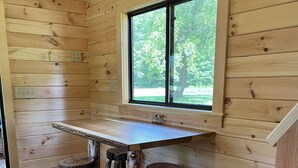 Een houten interieur met een bar, krukken en een raam met uitzicht op groen.