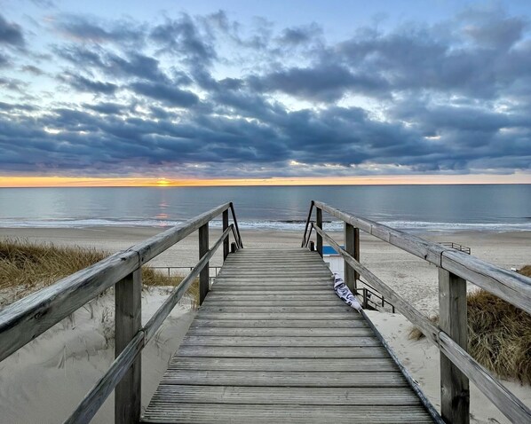 A wooden boardwalk leading to a beach with a cloudy sky.