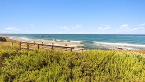 Une promenade en bois qui mène à une plage où l’eau est d’un bleu limpide et le ciel est dégagé.