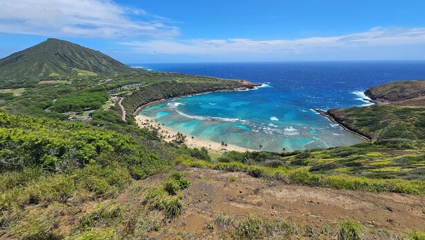 Paisagem costeira com montanha, mar azul cristalino e vegetação exuberante.