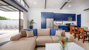 Een moderne woonkamer met een beige modulaire bank, een eethoek met houten stoelen, en een keuken met blauwe kastjes en roestvrijstalen apparatuur.