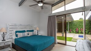 Een moderne slaapkamer met een groot bed, een plafondventilator en uitzicht op een tuin via een schuifdeur.