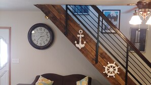 Una sala de estar con un sofá marrón, una escalera de madera, un reloj de pared y decoración de temática náutica.