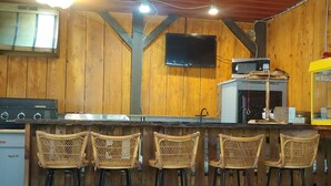 Zona de bar con paredes de madera, un televisor sobre la barra y un ventilador de techo.