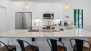 Une cuisine moderne avec des armoires blanches, des appareils en acier inoxydable, un comptoir en granit et des luminaires suspendus.