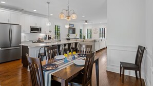 Une cuisine moderne avec des meubles blancs, des appareils en acier inoxydable et un coin repas comprenant des chaises en bois et un chemin de table à rayures.