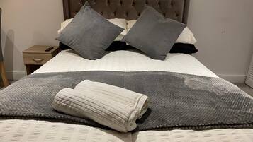 A neatly made bed with a grey and white blanket, a rolled-up towel, and two grey pillows.