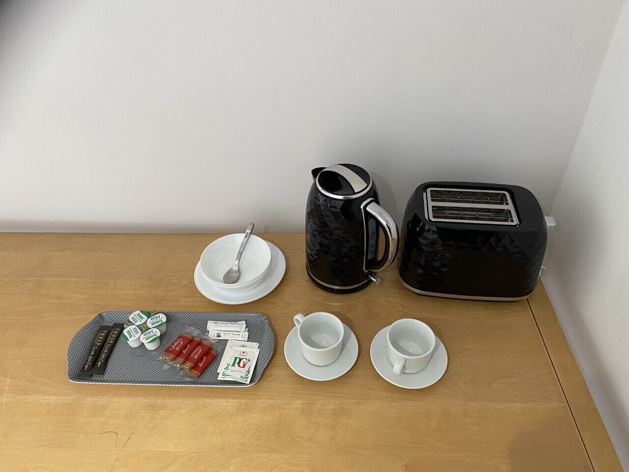 A breakfast setup with a tray, cups, a jug, and a toaster on a wooden table.
