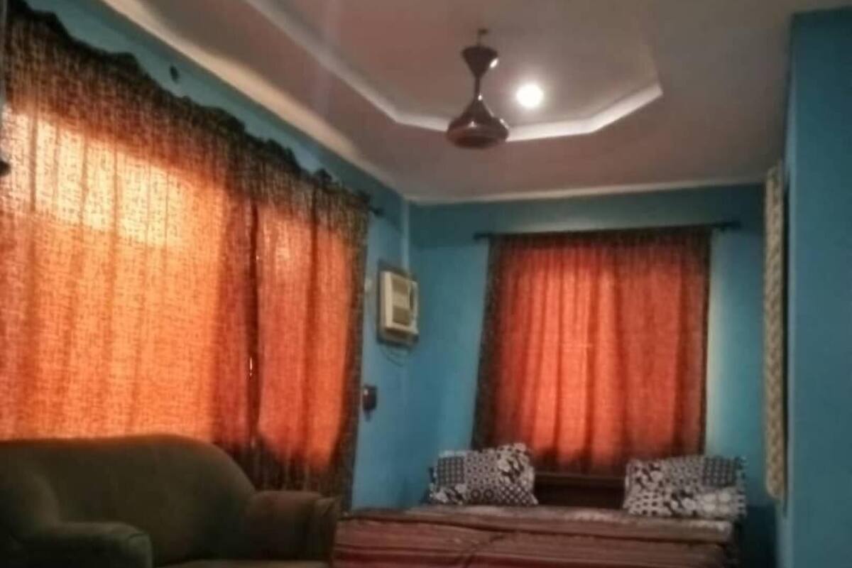 Une pièce comprenant un canapé, un lit avec une literie à motifs, un ventilateur de plafond et des rideaux.