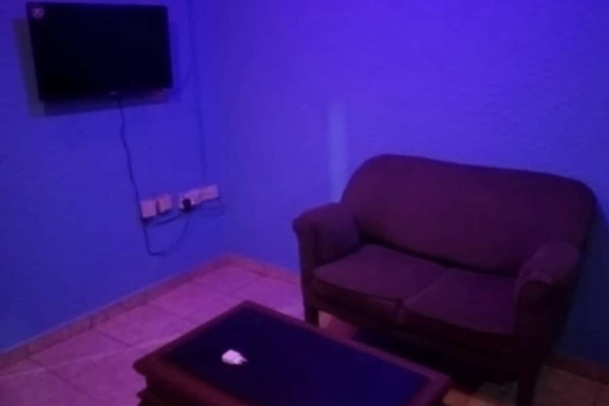 Une pièce comprenant un seul fauteuil et une petite table, un téléviseur fixé au mur et une prise de courant.