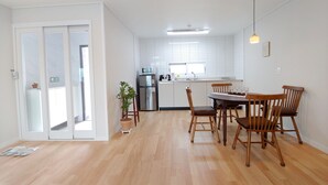 Une cuisine moderne avec des carreaux blancs, un réfrigérateur en acier inoxydable et un four à micro-ondes. On y trouve également un coin repas avec des chaises et une table en bois.
