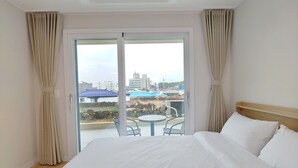 Une chambre d’hôtel avec un grand lit, un balcon avec une table et des chaises, et une vue sur la ville.