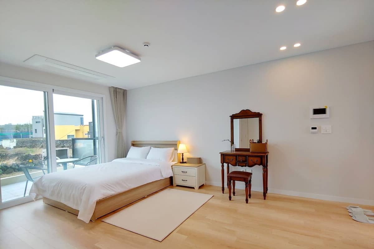 Un dormitorio con cama, mesita de noche, lámpara, cómoda, espejo y vistas al exterior.