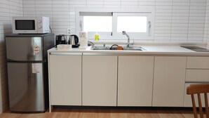 Une cuisine compacte avec des meubles blancs, un réfrigérateur en acier inoxydable, un four à micro-ondes, une machine à café et une fenêtre au-dessus de l’évier.
