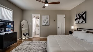 A bedroom with a bed, a desk with a computer, a ceiling fan, and artwork on the walls. - The Altitude Loft (Bartlesville)