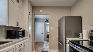A modern kitchen with white cabinets, a stainless steel refrigerator, a microwave, and a stove. - The Altitude Loft (Bartlesville)