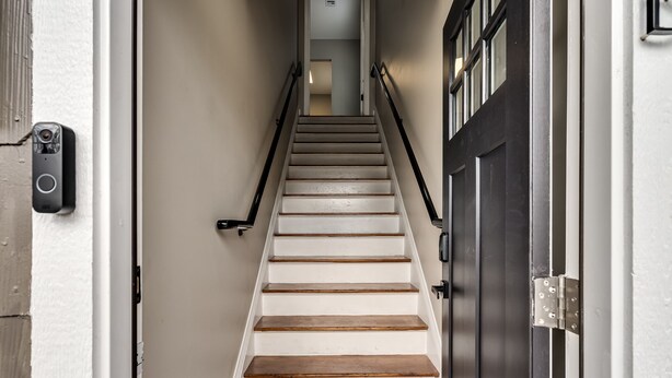 A staircase with wooden steps and a black handrail, leading to a door with a window. - The Altitude Loft (Bartlesville)