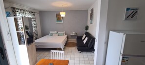 A compact bedroom with a bed, a black sofa, a small table, and a white refrigerator. - Fully equipped  - 5 minutes from the airport (Shuttle possible) (Les Abymes)